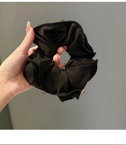 Detail of a black satin scrunchie with rhinestones held in hand against a solid wall