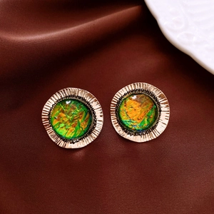 Macro detail of vintage round gold earrings with green resin insets on brown silk