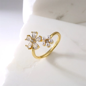 Bague fleur dorée ajustable avec zircon et perles blanches sur fond de marbre blanc
