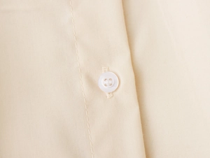 Nahaufnahme eines weißen Knopfes auf beige besticktem Stoff mit gewebter Textur