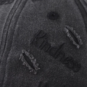 Close-up of Kindness embroidery and distressed ripped details on washed grey baseball cap