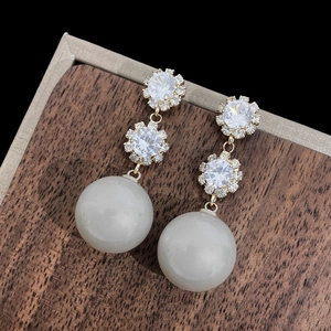 Détail de boucles d'oreilles géométriques avec perles blanches et fleurs en strass brillants