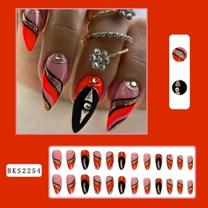 Detail view of long stiletto press-on nails in orange, black, and pink with gold glitter