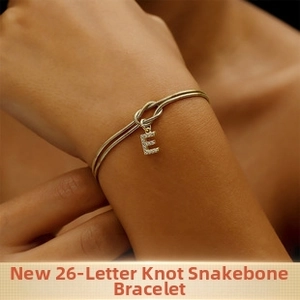 Dettaglio del bracciale a serpente dorato con ciondolo lettera E in pavé e nodo centrale