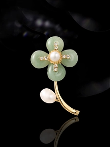 Detail of flower brooch featuring green jade petals and white pearl center on dark reflective background