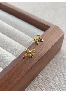 Detail view of gold bow-knot stud earrings featuring a polished 3D ribbon design