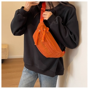 Detail of orange canvas chest bag with white letter embroidery and woven rope zipper pull
