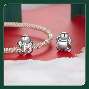 Macro shot of silver gingerbread man charm with green enamel and pink gemstone detail