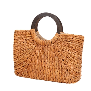 Natural corn husk woven tote bag with round wood handles on white background