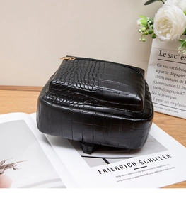 Detail of black crocodile pattern backpack with golden zipper on a wooden table setup