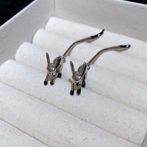 Close-up of rabbit-shaped silver needle earrings with black enamel details on a jewelry tray