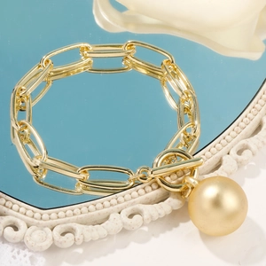 Detailed shot of golden chunky chain bracelet with ball pendant on reflective mirror