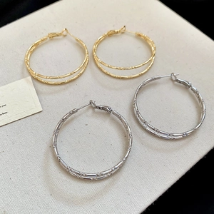 Detail of bamboo joint double-hoop earrings in gold and silver finish on beige fabric