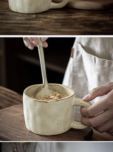 Close-up of a hand holding a rustic beige ceramic mug with a matching spoon in a cozy setting