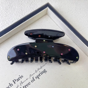 Close-up of black acetate hair claw clip with colorful rhinestones on a textured background