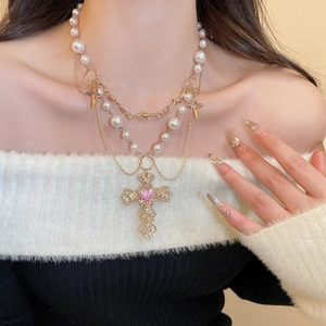 Detail of layered gold necklace featuring a baroque cross with a pink heart and pearls