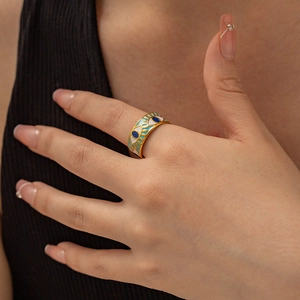 Detail of a vintage gold Evil Eye enamel ring worn on a finger with a black background