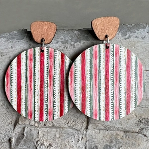 Macro shot of striped wooden drop earrings in festive red, white, and green on grey stone