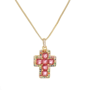 Gold cross necklace with colorful zircon gemstones and pink center crystals on white background