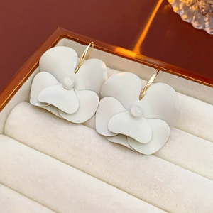 Macro detail of white layered flower earrings with stamens in a beige velvet jewelry box