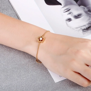 Detailed view of a gold star charm bracelet with a crystal center on a model's wrist