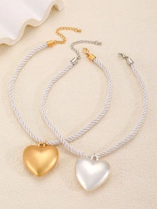 Détail des pendentifs cœur en or et argent avec colliers en soie blanche tressée