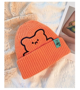 Detail of orange knit beanie with black bear embroidery and mint green label on lace
