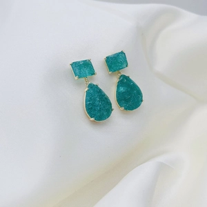 Detail of green teardrop silver earrings with gold plating on white fabric