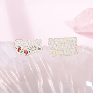 Close-up of Stay Wild and I Can't Adult Today pins in white seashell tray