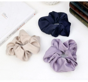 Detailed view of three satin scrunchies in navy, beige, and lavender with twill texture