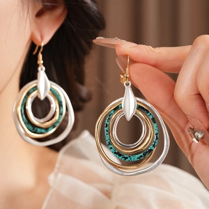 Close-up of layered round earrings with turquoise accents and silver leaf pendant
