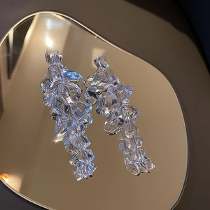Artistic detail of irregular acrylic ice earrings reflecting on a mirror surface