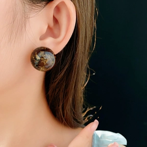 Detail of round amber resin stud earring with gold leaf flakes on model ear lobe