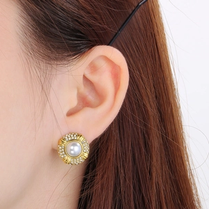 Detailed close-up of an oval 18k gold stud earring with pearl and crystal halo on ear