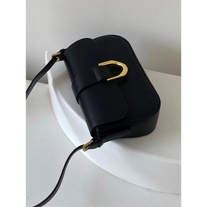 Detail of minimalist black leather shoulder bag with polished gold horseshoe buckle closure