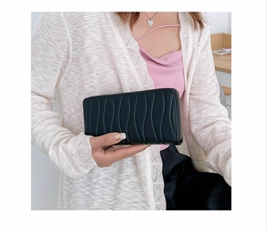 Close-up of black long purse with wave texture and gold zipper held in hand