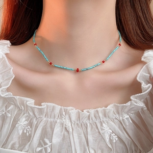 Detail of bohemian beaded necklace with blue and red stones on a model's collarbone