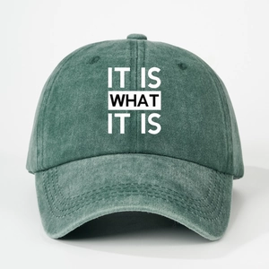 Close-up of washed green denim baseball cap with white IT IS WHAT IT IS printed text