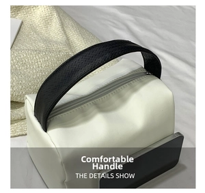 Detailed view of white minimalist handbag with black woven handle and zipper closure