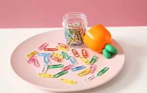 Close-up of carrot-shaped stationery container with colorful metal paper clips on a tray