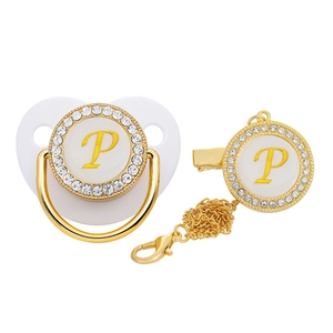 Close-up of white baby pacifier and clip with gold letter P and sparkling crystal rhinestones