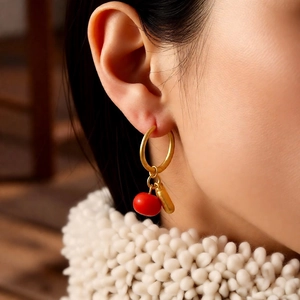 Close-up of elegant gold hoop earrings with red bead pendant on model wearing white sweater