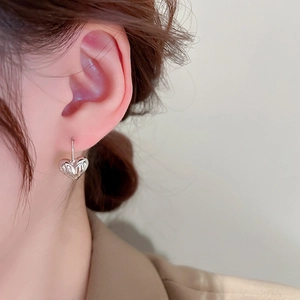 Close-up of silver textured heart-shaped earrings on a model with minimalist style