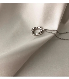 Macro shot of 925 silver oval donut pendant necklace on white luxury silk fabric