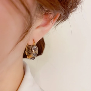 Close-up of golden hoop earring featuring a grey-purple cat eye stone and pavé zircons