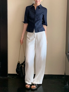 Détail d'une chemise en lin bleu foncé associée à un pantalon blanc à taille haute chic