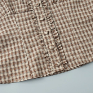 Detail of coffee plaid shirt featuring ruffle trim and matching fabric buttons