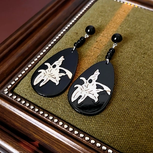 Macro detail of retro drop earrings with white cutout patterns on a black base