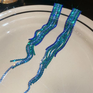Macro shot of long sparkling blue and green gradient rhinestone tassel earrings in a dish