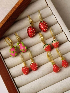 Detail of five strawberry and dragon fruit dangle earrings in a beige velvet jewelry box